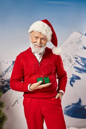 fröhlicher Weihnachtsmann hält Geschenk mit einer Hand in der Tasche vor verschneiter Kulisse, Winterkonzept