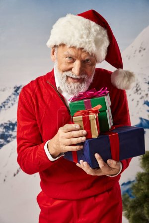 hombre barbudo alegre vestido como Santa con sombrero navideño sosteniendo pila de regalos, concepto de invierno