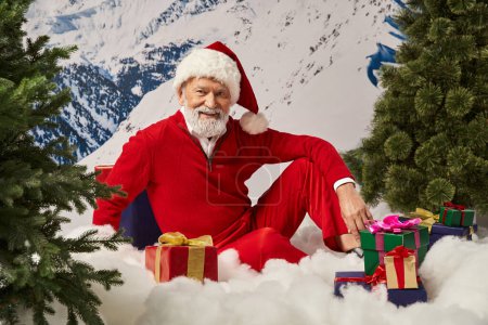 happy Santa sitting on snow surrounded by many presents and smiling at camera, Merry Christmas