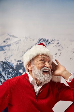 portrait of white bearded jolly Santa in red festive hat posing with hand near face, winter concept