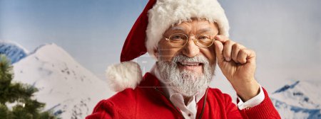 cheerful man in Santa costume with glasses on looking straight at camera, winter concept, banner