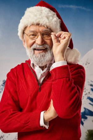 stylischer gut aussehender Mann im Weihnachtsmannkostüm, der mit Brille und verschränkten Armen posiert, Frohe Weihnachten