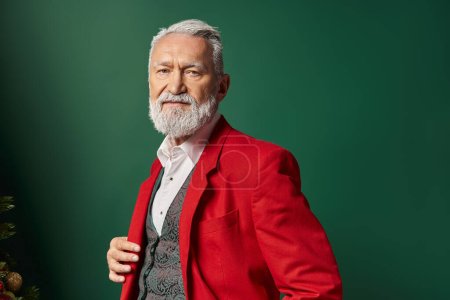 portrait of stylish man in red Santa suit looking at camera on green backdrop, winter concept