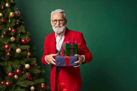 Eleganter Weihnachtsmann mit Brille und Bart, stapelweise Geschenke vor dunkelgrünem Hintergrund, Winterkonzept