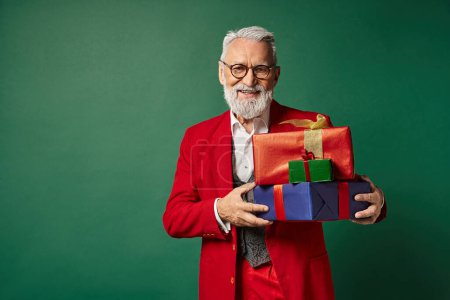 fröhlicher Weihnachtsmann mit Brille, der mit einem Stapel von Geschenken posiert und in die Kamera lächelt, Weihnachtskonzept