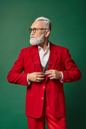 handsome man dressed as Santa with glasses fastening buttons on suit looking away, winter concept