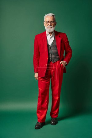 classy man dressed as Santa posing with one hand in pocket on green backdrop, winter concept