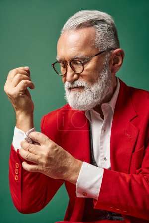 portrait of elegant Santa with beard and glasses fastening button on his sleeve, winter concept