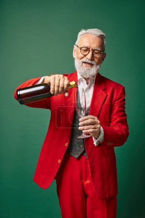 alegre Santa con barba blanca vertiendo copa de flauta con champán sobre fondo verde, concepto de invierno