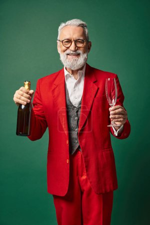 Glücklicher Weihnachtsmann mit Brille und Bart im roten Anzug posiert mit Champagnerflasche, Winterkonzept