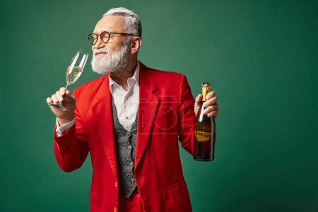 elegant Santa with beard in red classy suit testing champagne on green backdrop, winter concept