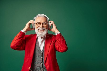 cheerful handsome Santa with white beard and glasses putting on big headphones, winter concept