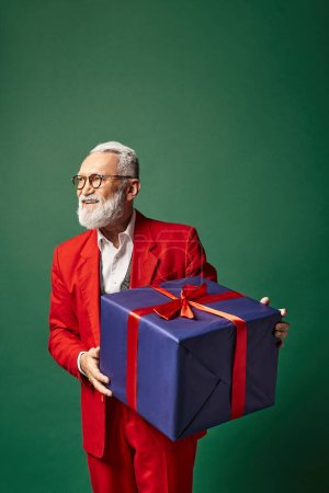 stilvoller Weihnachtsmann mit riesigem Geschenk auf grünem Hintergrund und wegschauendem, winterliches Konzept