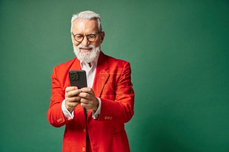 alegre hombre elegante en traje rojo con gafas y barba sonriendo en el teléfono móvil, concepto de invierno