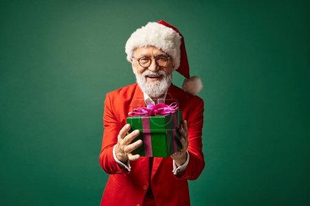 élégant beau Père Noël posant avec présent dans les mains souriant sincèrement à la caméra, concept d'hiver