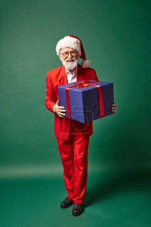 eleganter Weihnachtsmann mit Weihnachtsmütze und riesigem blauem Geschenk mit Schleife, Winterkonzept