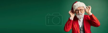 Téléchargez les photos : Beau Père Noël barbu blanc touchant son chapeau rouge et regardant la caméra, concept d'hiver, bannière - en image libre de droit