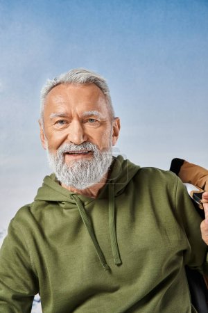 joyous Santa with white beard looking at camera with snowy mountain on backdrop, winter concept