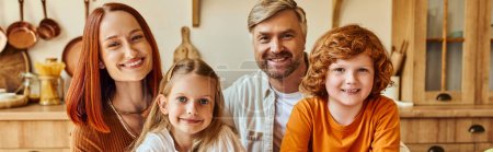 freudige Eltern mit Sohn und Tochter, die in der Küche in die Kamera schauen, Familienporträt zu Hause, Banner