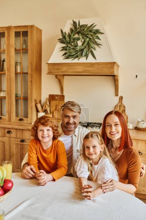 Lächelnde Eltern mit Sohn und Tochter, die in der Küche in die Kamera schauen, glückliches Familienporträt zu Hause
