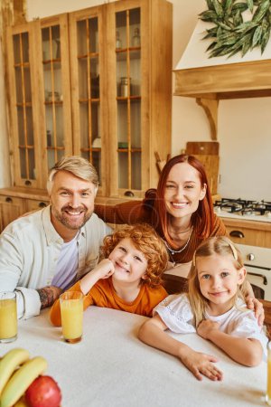 parents with adorable kids looking at camera near during breakfast in cozy kitchen, smiling faces