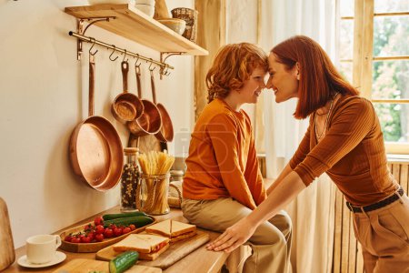 joyful kid on kitchen counter near sandwiches and fresh vegetables face to face with smiling mother
