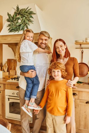 cheerful parents with adorable kids looking at camera in cozy modern kitchen, emotional connection