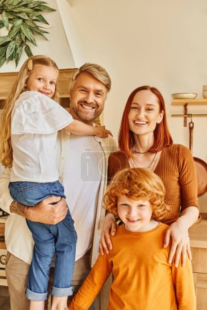 joyful parents with adorable kids looking at camera in cozy modern kitchen, emotional connection