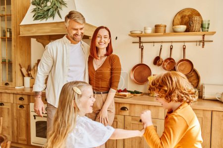 joyful parents looking at excited kids playing and having fun in kitchen, siblings relationship