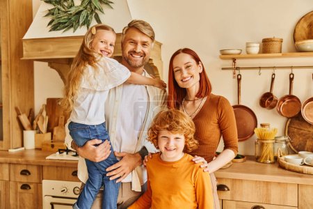 joyful children with smiling parents looking at camera in modern kitchen, cozy home environment