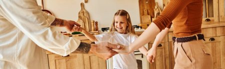 Foto de Alegre chica cogida de la mano y jugando con los padres en acogedora cocina, diversión y risa, pancarta - Imagen libre de derechos