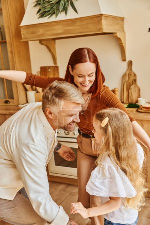 Foto de Padres alegres con adorable hija divirtiéndose y jugando en acogedora cocina, momentos de unión - Imagen libre de derechos