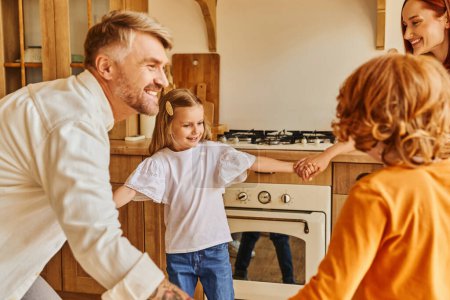 glückliche Eltern mit unbeschwerten Kindern, die sich beim Spielen in der Küche an den Händen halten, gepflegte Erinnerungen