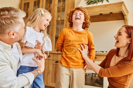 Glückliche Eltern kitzeln überglückliche Kinder in der modernen Küche, Spaß und Lachen in gemütlicher häuslicher Umgebung