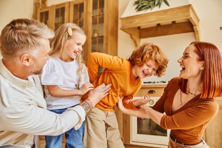 Téléchargez les photos : Parents joyeux chatouillant enfants excités dans la cuisine moderne, amusant et rire dans un environnement confortable à la maison - en image libre de droit