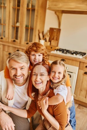 overjoyed parents and children embracing and looking at camera in cozy kitchen, cherished moments