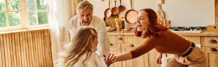 excited parents playing with happy daughter in modern kitchen at home, family interaction, banner