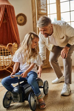Foto de Padre cariñoso ayudar a la hija feliz montar coche de juguete en la acogedora sala de estar en casa, jugando juntos - Imagen libre de derechos