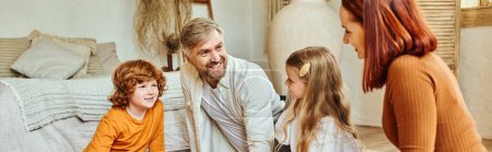 joyful parents with daughter and son looking at each other in living room at home, horizontal banner