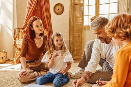 glücklicher Mann nähert sich glücklicher Familie, während er auf dem Boden im gemütlichen Wohnzimmer sitzt, kreative Aktivitäten