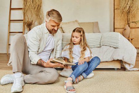 Téléchargez les photos : Homme tatoué livre de lecture à fille attentive sur le sol dans une chambre confortable, apprendre ensemble - en image libre de droit