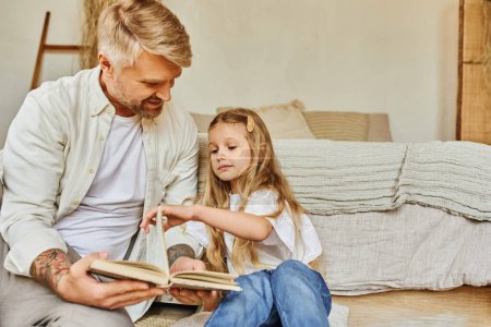 Téléchargez les photos : Heureux père et adorable fille assis sur le sol dans la chambre et le livre de lecture, apprendre ensemble - en image libre de droit