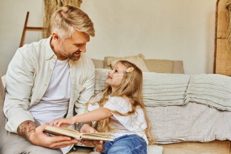 Photo for Cheerful father and cute daughter sitting on floor in bedroom and reading book, learning together - Royalty Free Image