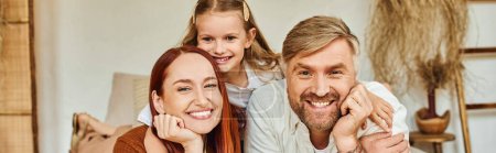 Photo for Joyful parents with carefree daughter relaxing in bedroom and looking at camera, horizontal banner - Royalty Free Image