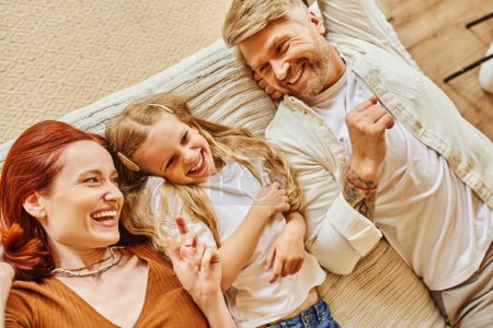Photo for Top view of cheerful parents with cute daughter lying down and having fun on bed, relaxation time - Royalty Free Image