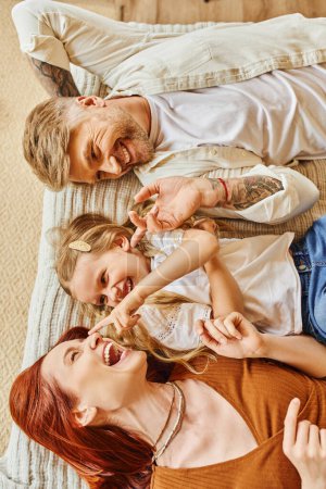 top view of joyful parents with cute daughter lying down and having fun on bed, relaxation time