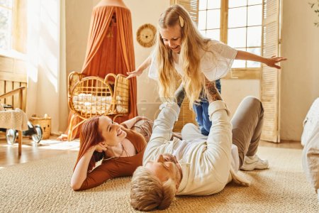 Foto de Mujer alegre mirando marido jugando con hija en piso en sala de estar, momentos de unión - Imagen libre de derechos