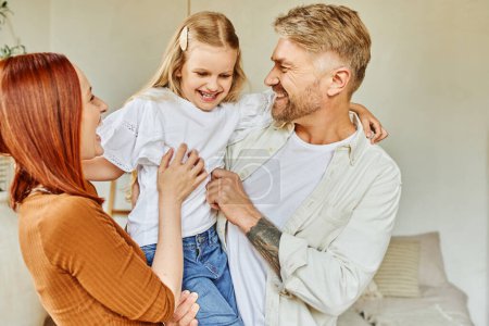Photo for Excited husband and wife holding and tickling daughter in bedroom at home, fun and laughter - Royalty Free Image