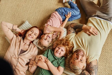 Photo for Top view of smiling parents and children lying down on floor in living room and smiling at camera - Royalty Free Image