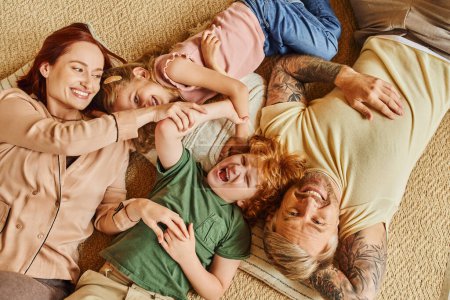 Téléchargez les photos : Vue de dessus des parents heureux et des enfants couchés et sur le sol et riant dans le salon moderne - en image libre de droit